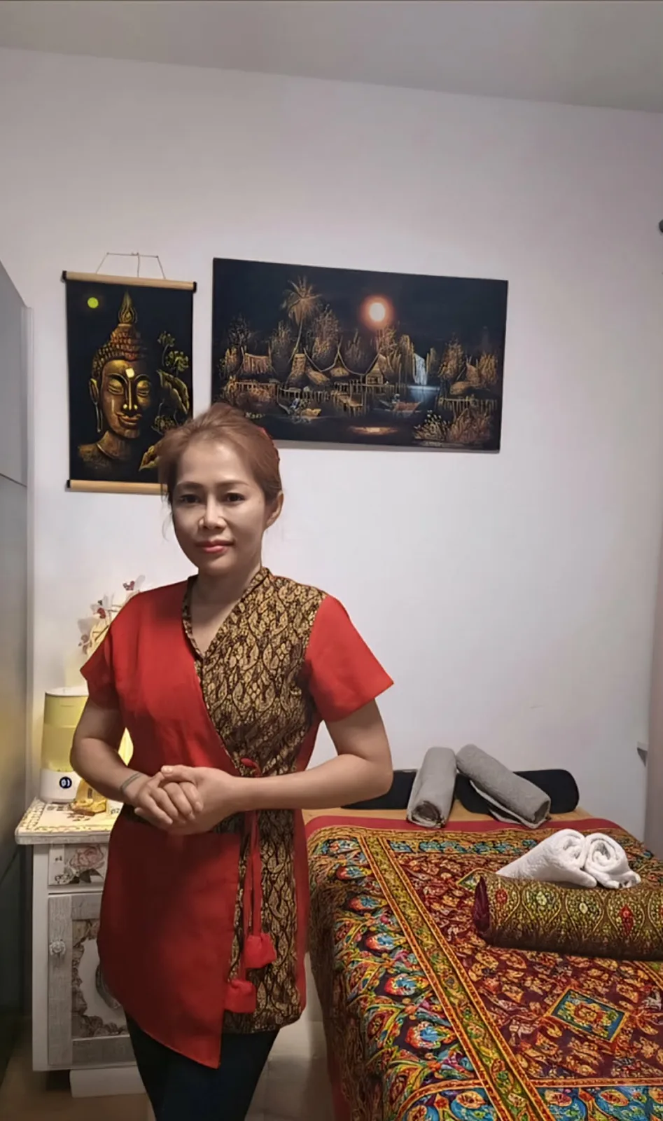 Apisara Pober im roten Thai-Kleid vor der Massageliege