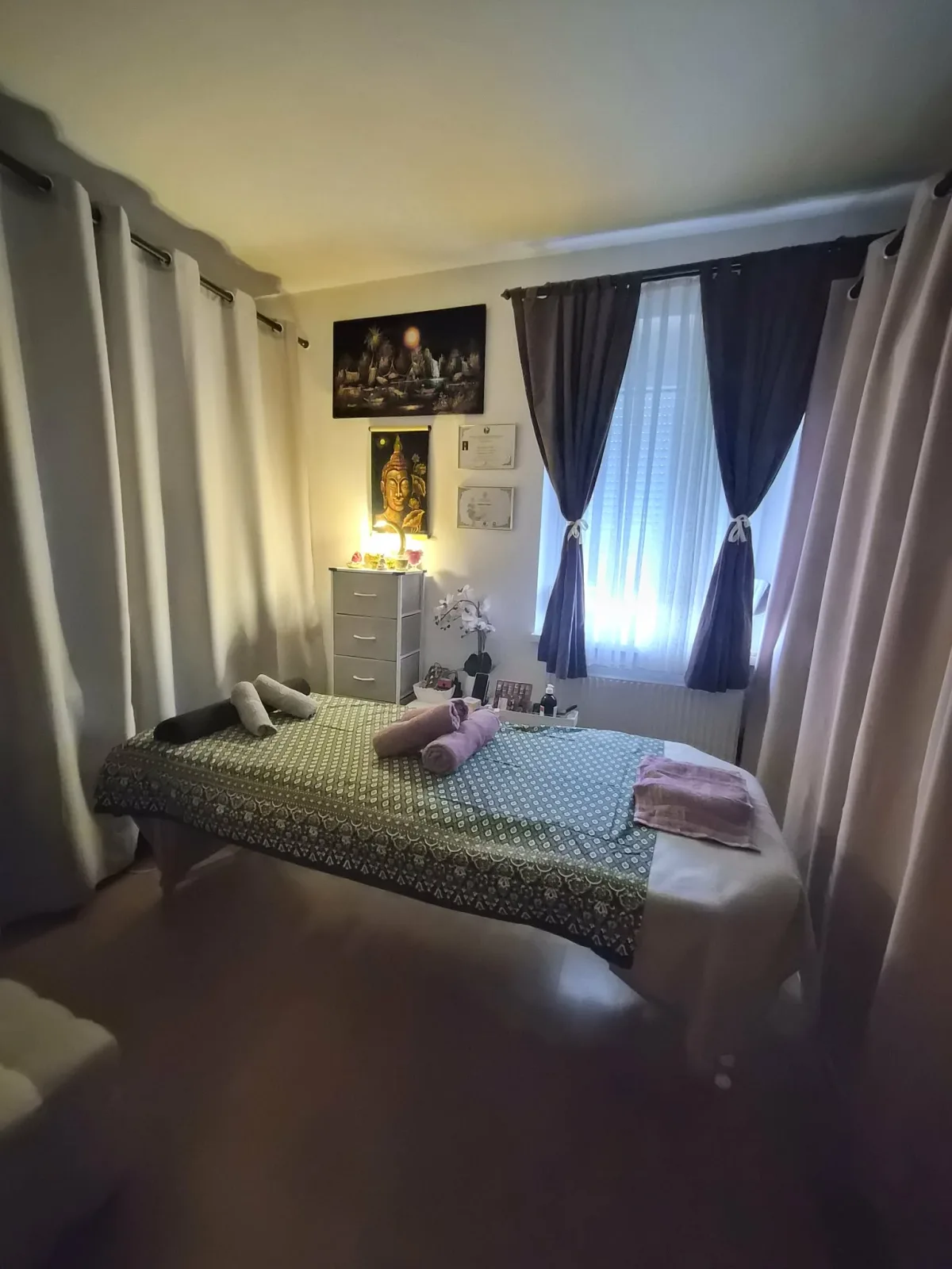 Behandlungsraum mit Liege, Vorhängen und Buddha-Bild
